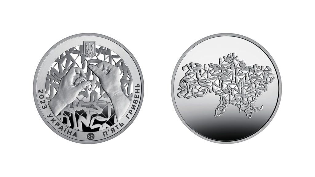 The front and back sides of a silver coin. One side depicts hands weaving a camouflage net, and the other depicts a camouflage net in the shape of Ukraine.