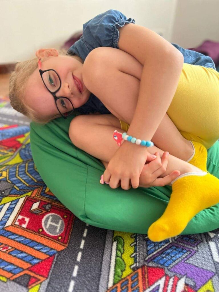 A girl lies on her side on a beanbag and hugs her legs to her chest, smiling.