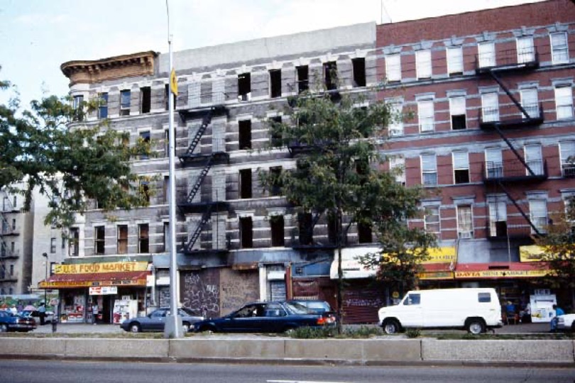 A street in Harlem, New York City.  There is a five-story building in the background and cars in the midground.