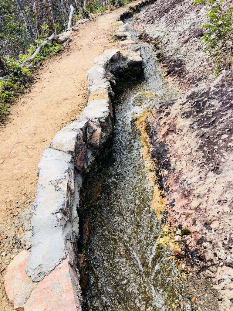 A stream with a concrete wall on the left side and a rock face on the right.