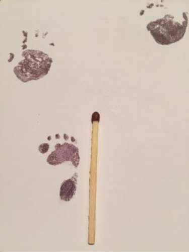 A white background with ink handprints and footprints next to a matchstick for scale. The footprint is about half the length of the matchstick. 